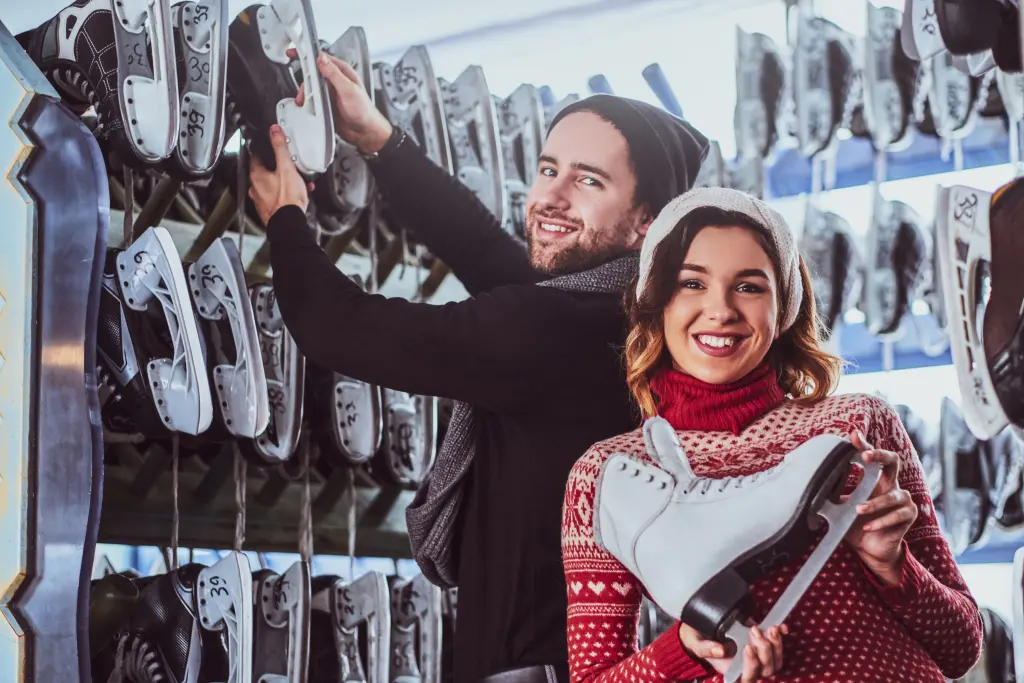 young-couple-wearing-warm-clothes-standing-near-rack-with-many-pairs-skates-choosing-his-size.jpg